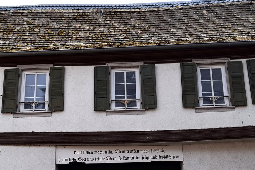 Deutscher Text auf traditioneller Fassade über den Glauben an Gott und die Freude am Wein von Studio LE-gals