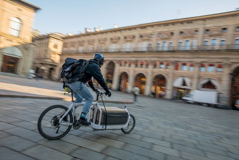 Zusteller auf einem Fahrrad auf dem Piazzo Maggiore in großer Eile von Joost Adriaanse