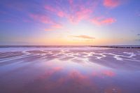 Le ciel rouge du soir se reflète sur le sable mouillé de la plage.