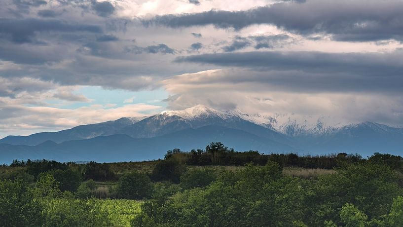 Sonnenbeschienener, schneebedeckter Gipfel der französischen Pyrenäen unter einem bedrohlichen Wolkenhimmel. von Haarms