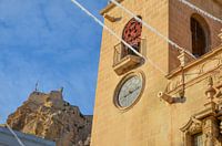 Kunstvoller Uhrenturm der Basilika Santa Maria von Alicante. Im Hintergrund das Castillo de Santa Bá