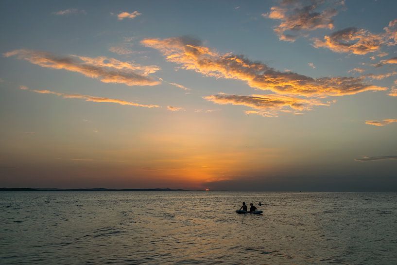 People on a raft staring at the setting sun by Menno van der Haven