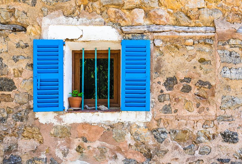 Detail view of stone wall and window with blue shutters of house by Alex Winter