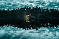 Leuchtende Hütte am spiegelnden See mit dramatischem Himmel