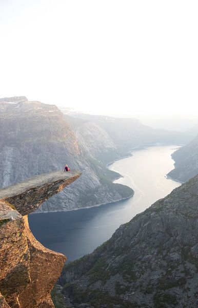 Eine Person sitzt bei Sonnenuntergang auf der Trolltunga in Norwegen von Guido Boogert