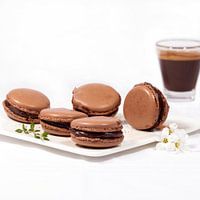 Hausgemachte Schokoladen-Macarons auf einem weißen Teller und eine Tasse Expresso