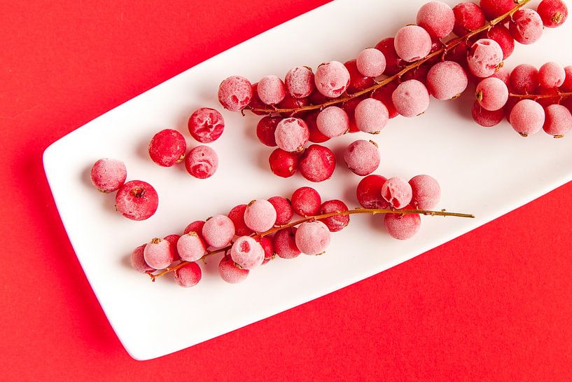 Red berries with ripe fruit on a white plate against a red background. by Ans van Heck