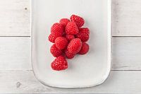 Himbeeren auf einem Teller auf einer Holzunterlage.