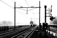 Zwart-wit foto van een Hollandse trein in mist bij spoorwegovergang