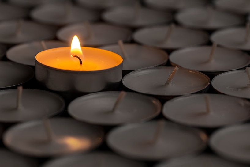 Einzelne Flamme zwischen dunklen Teelichtern von Alexander Baumann