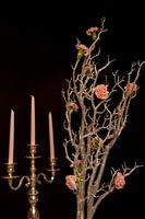 Vintage candlestick with candles and pink flowers on black background. Still life floral arrangement