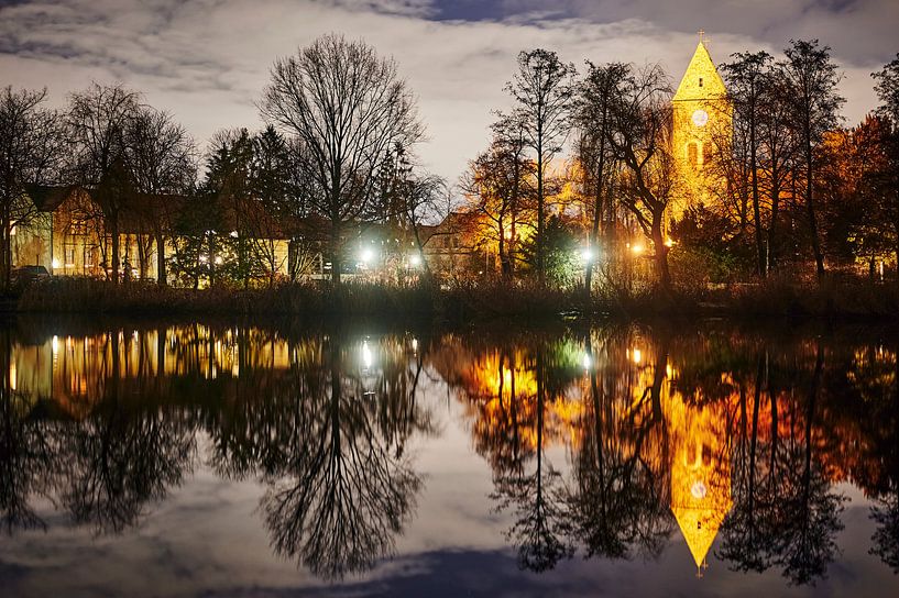 Eine historische Dorfkirche, die in der Nacht von Lampen angestrahlt wird und sich in einem Teich sp von Michaela Bechinie