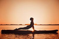 Yogapose comme silhouette au coucher du soleil sur une planche de surf