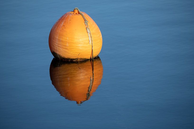 Orangefarbene Boje mit Spiegelung im blauen, ruhigen Wasser eines Sees, Konzept für Entspannung, Pau von Maren Winter