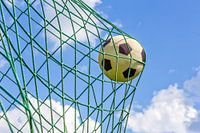 Voetbal in net van goal tegen blauwe lucht