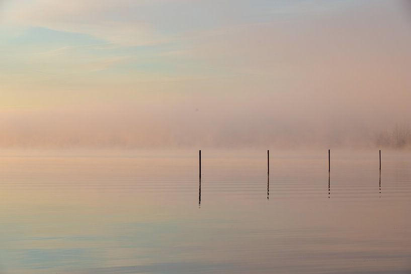 lever de soleil brumeux sur l'eau avec des poteaux réfléchissants et des couleurs pastel par Kim Willems