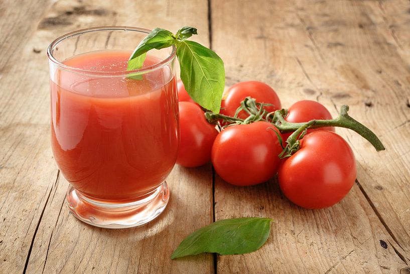 fresh organic tomato juice in a drinking glass with pepper and basil garnish on a rustic wooden boar by Maren Winter