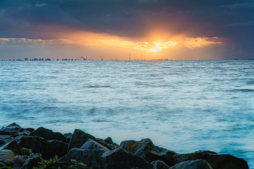 Skyline von Amsterdam bei bewölktem Sonnenuntergang mit Sonnenstrahlen über der Oberfläche des IJsselmeers von Fotografiecor .nl