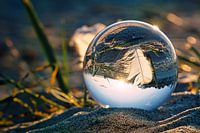 Sphère en verre sur la plage de Zingst. Une plume se reflète dans la sphère.