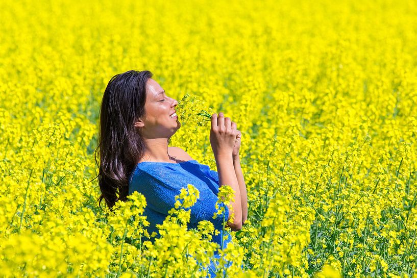 Young colombian woman smelling yellow flowers in agricultural  rapeseed field by Ben Schonewille