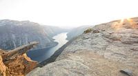 Someone walks over the famous Trolltunga in Norway at the last rays of sunshine