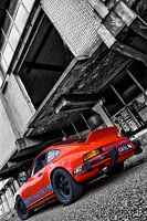 Orangefarbener Porsche 911 vor baufälligem Anwesen in schwarz-weiß