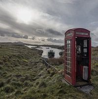 Altmodische Telefonzelle in leerer Landschaft mit Boot im Hintergrund