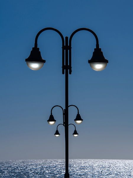 Three lanterns in a row with the ocean in the background by Harrie Muis