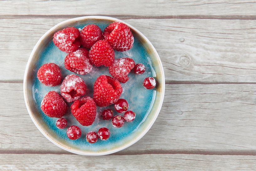 Raspberries and redcurrants on a plate on a wooden base. by Ans van Heck