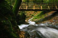 Schnell fließender Fluss unter einer Holzbrücke.