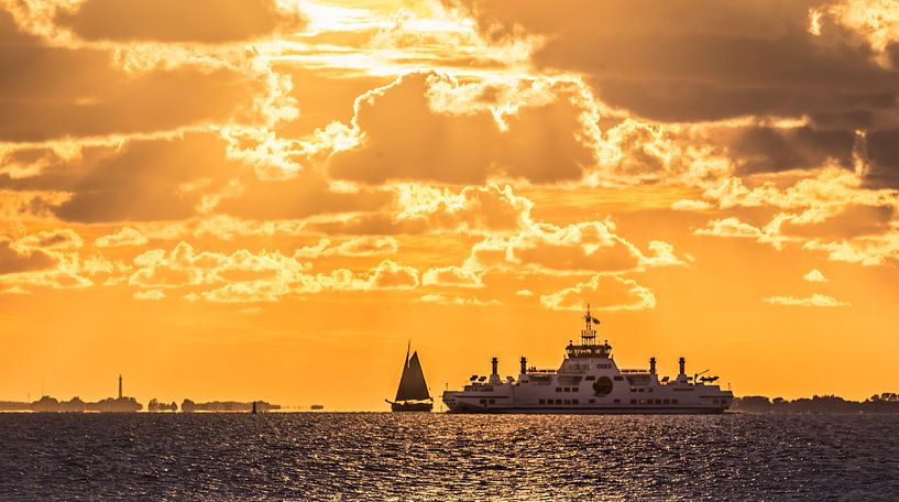 Sunset with sailboat and ferry on the mud flats by Martijn van Dellen