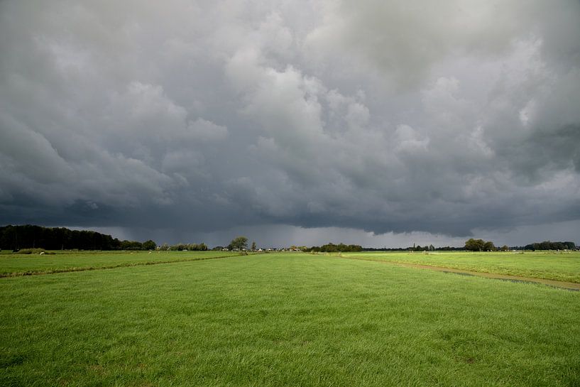 Ominous dark thunderclouds above green polder landscape by Arjen Tjallema