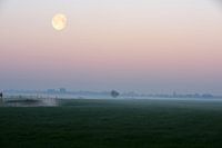 Nebliger Sonnenaufgang in der niederländischen Landschaft mit Kanal in den Feldern und dem Mond