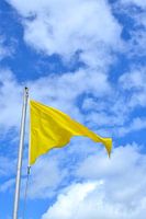 Drapeau jaune flottant devant un ciel bleu avec des nuages
