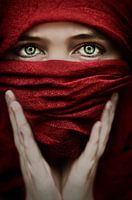 Indringende Foto van Vrouw in Rode Sluier - Krachtige Blik met Groene Ogen (gezien bij vtwonen)