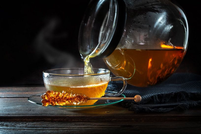 Hot steaming tea is poured from a pot into a glass cup, served with a stick of rock candy, motion bl by Maren Winter