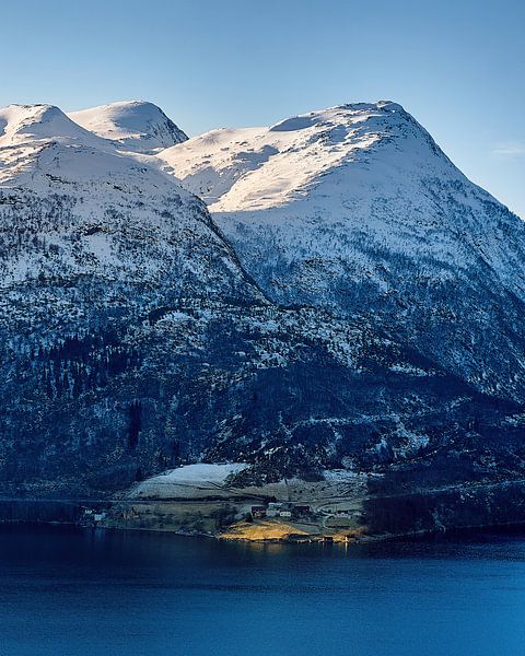 Le soleil illumine une petite ferme au-dessous des montagnes imposantes. par qtx