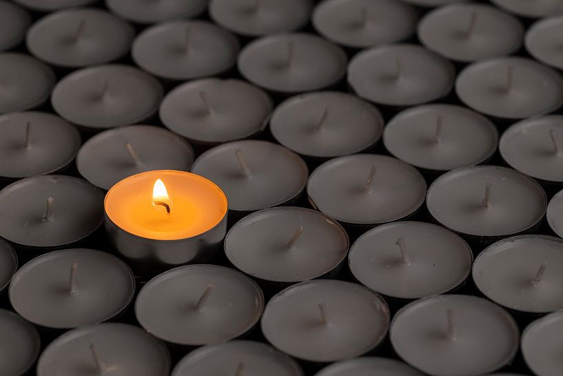 Einzelne Kerze zwischen dunklen Teelichtern von Alexander Baumann