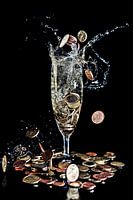 Geldmünzen fallen in ein Champagnerglas vor schwarzem Hintergrund